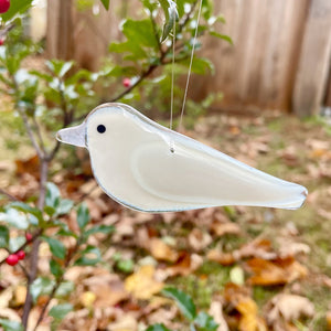 Glass white dove hanging ornament hanging outdoors with a holly bush with red berries in the background
