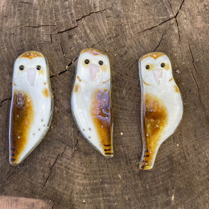 Three owl-shaped fused glass ornaments on a wooden surface