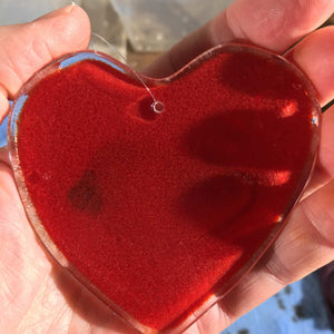 A Fused Glass Heart with Chickadee being held in a hand in Reverse