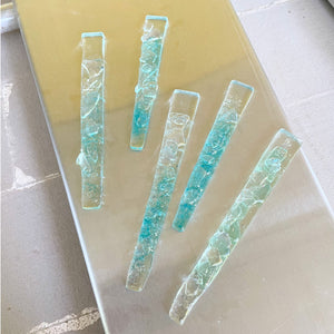Set of five rectangular turquoise glass icicles on a metal kiln lid background
