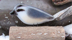 A fused glass nuthatch bird sits on a wooden log. It's a snowy scene