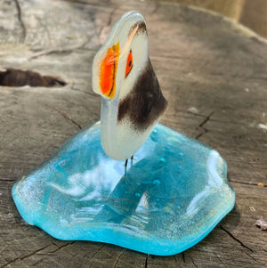 Side view of a fused glass puffin on an glass iceberg. The ornament is on a tree stump.