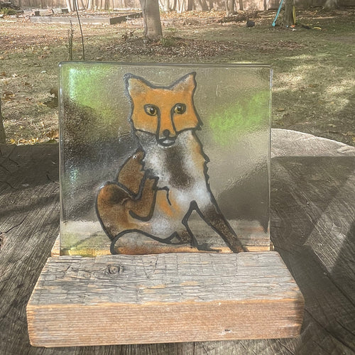 Glass panel with a fox design on a wooden stand outdoors
