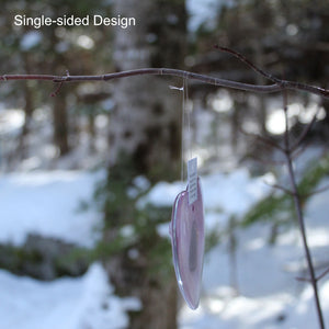 A small glass pink heart is hanging side on to the viewer. In the background is a snowy nature scene