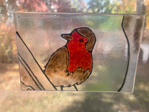 Stained glass panel with a red and brown bird design, outdoors.