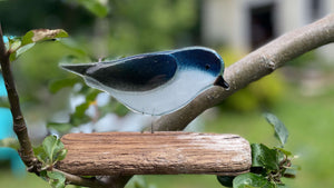 a fused glass tree swallow is resting on driftwood in a tree branch