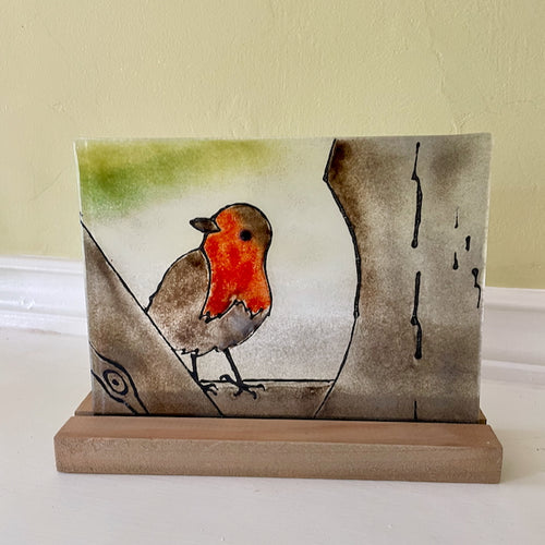 Decorative fused glass piece with a robin design on a stand against a plain background