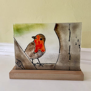 Decorative fused glass piece with a robin design on a stand against a plain background