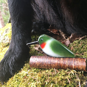 A red and green glass ruby throated hummingbird sits in front of some black dog legs