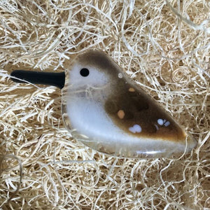 A close up of a brown and white speckled glass bird in a "nest".