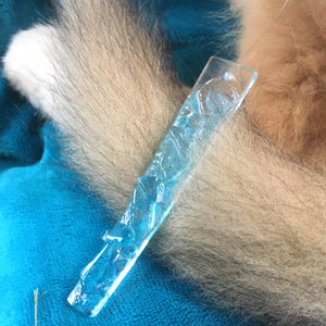 Glass icicle christmas ornament on a puppy tailwith blue fabric in the background