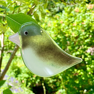 Grey and White glass Junco bird ornament hanging from a tree with a blurred green foliage background