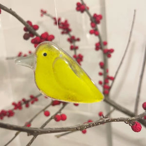 A lemongrass yellow glass chick hangs from a branch with red berries