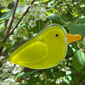 Yellow glass bird ornament hanging among green leaves and white flowers