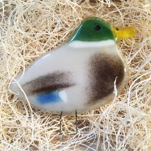 Load image into Gallery viewer, A glass mallard duck ornament is laying on wood fibre nesting material
