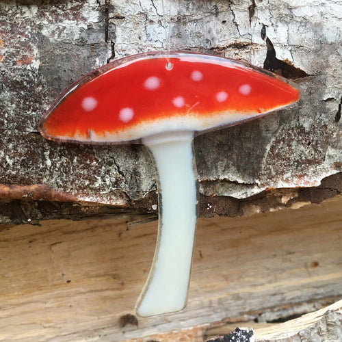 Fused Glass Red mushroom with white spots hangs in front of some bark