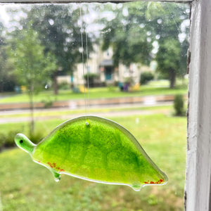 A fused glass painted turtle hangs in a window.