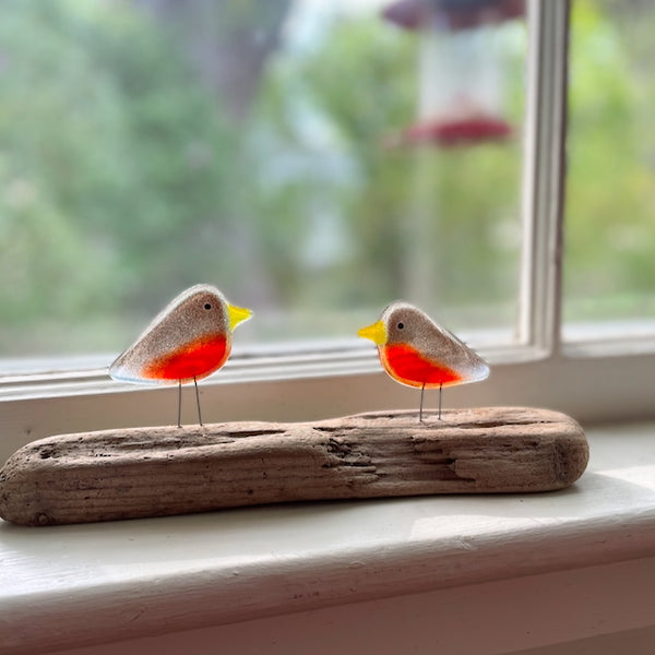 Load image into Gallery viewer, Perched pair of Robin Chicks made from fused glass, on driftwood. Red and brown glass. Displayed on a window sill.
