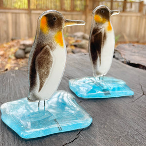 Two glass penguin figurines on a wooden surface with a blurred natural background.