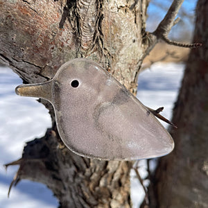 pink glass bird shaped ornament attached to a tree branch with a snowy background