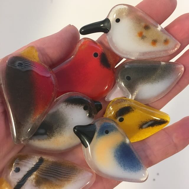 Eight glass pocket birds sit in the palm of a hand