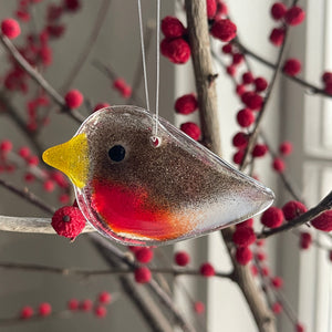 Decorative glass robin ornament hanging among red berries