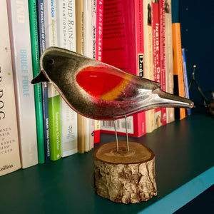 Glass red winged blackbird perches on a shelf in front of a library full of dog books