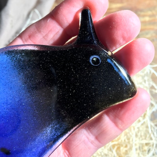 a close up of a sparkly glass steller's jay head in the palm of the artist's hand