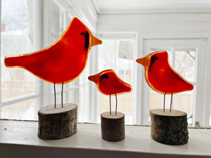 Three red bird figurines on wooden bases in a bright room with large windows.