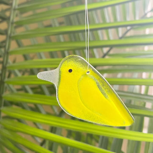 A glass lemongrass yellow chick hangs in front of a tropical palm