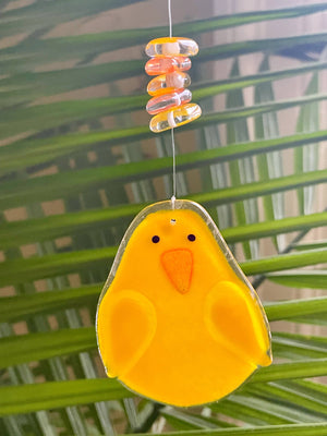 A bright yellow hanging glass chick is dangling in front of a tropical palm plant