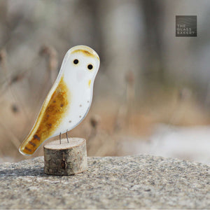 a brown and white fused glass barn owl sits on a log on a rock