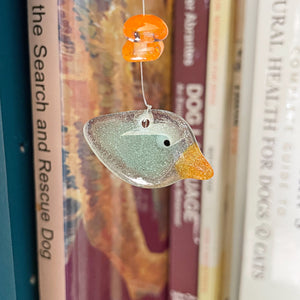 Decorative bird ornament hanging among books on a shelf