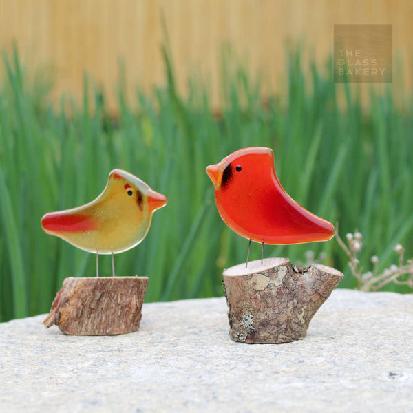 Load image into Gallery viewer, two glass bird ornaments perch on logs on top of a rock. The birds are a male and female.
