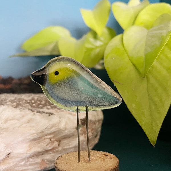Charger l'image dans la galerie, Glass bird figurine on a wooden base with green leaves in the background
