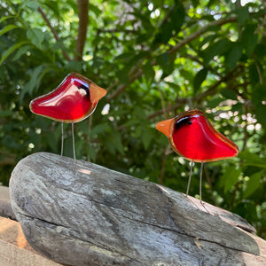 A pair of small red cardinals made from fused glass sit on a log