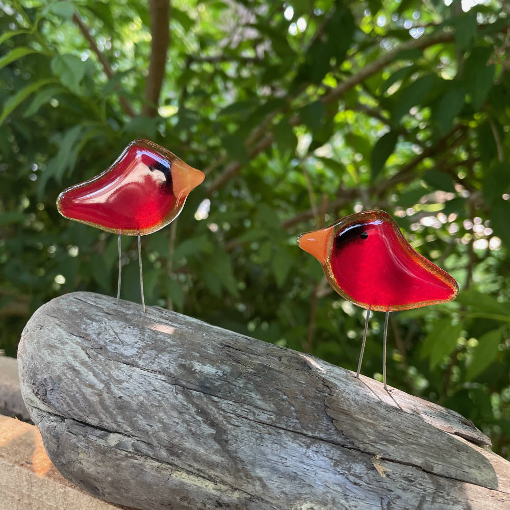 A pair of small red cardinals made from fused glass sit on a log