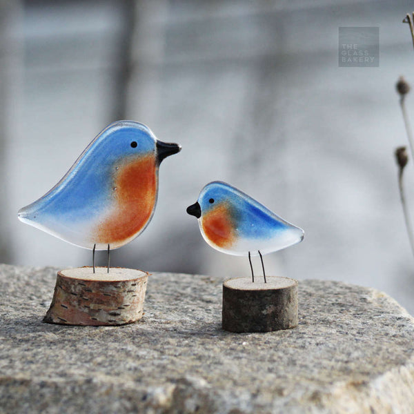 Load image into Gallery viewer, a pair of different sized bluebirds on log perches sit on a rock
