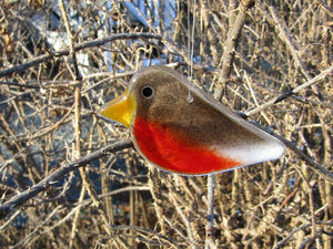 A fused glass robin chick hangs in a  thorny rose bush in winter