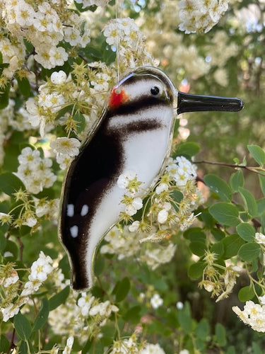 a fused glass hairy woodpecker hangs in front of white flowers