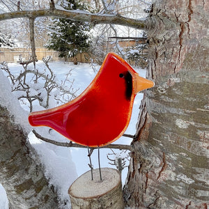 Red glass cardinal bird ornament on a tree branch with a snowy background