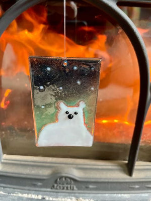 A glass tile featuring a white polar bear on a midnight blue background with snowflakes, hangs in front of a roaring fire.