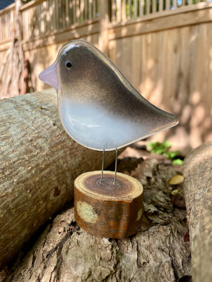 A grey and white fused glass adult junco perched on a log