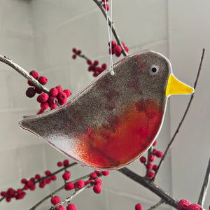 Decorative glass adult robin ornament hanging on a branch with red berries.