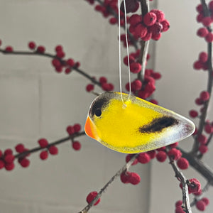 Decorative yellow goldfinch bird ornament hanging on a branch with red berries