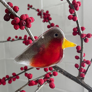 Decorative glass robin hanging among red berries on a branch.