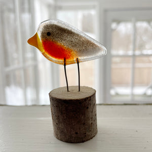 Glass robin bird figurine on a wooden base with a blurred indoor background