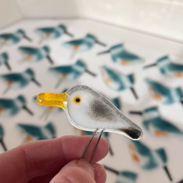 a small glass seagull bird with out of focus kingfishers in the background