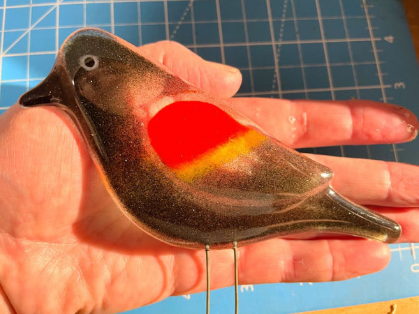 Load image into Gallery viewer, a fused glass red winged blackbird is held in the hand for scale.
