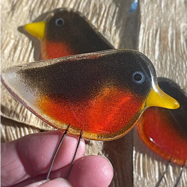 Load image into Gallery viewer, Glass bird ornament with a red breast and yellow beak held by a hand against a textured beige background.
